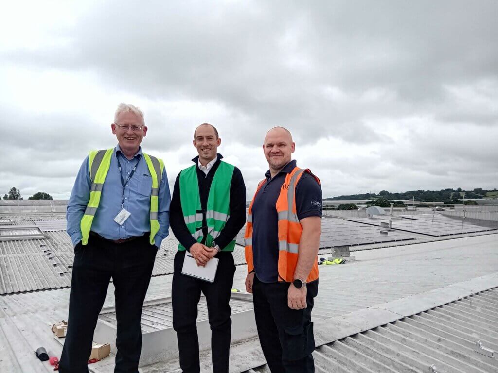 Picture showing three people standing on roof with solar panels in the background