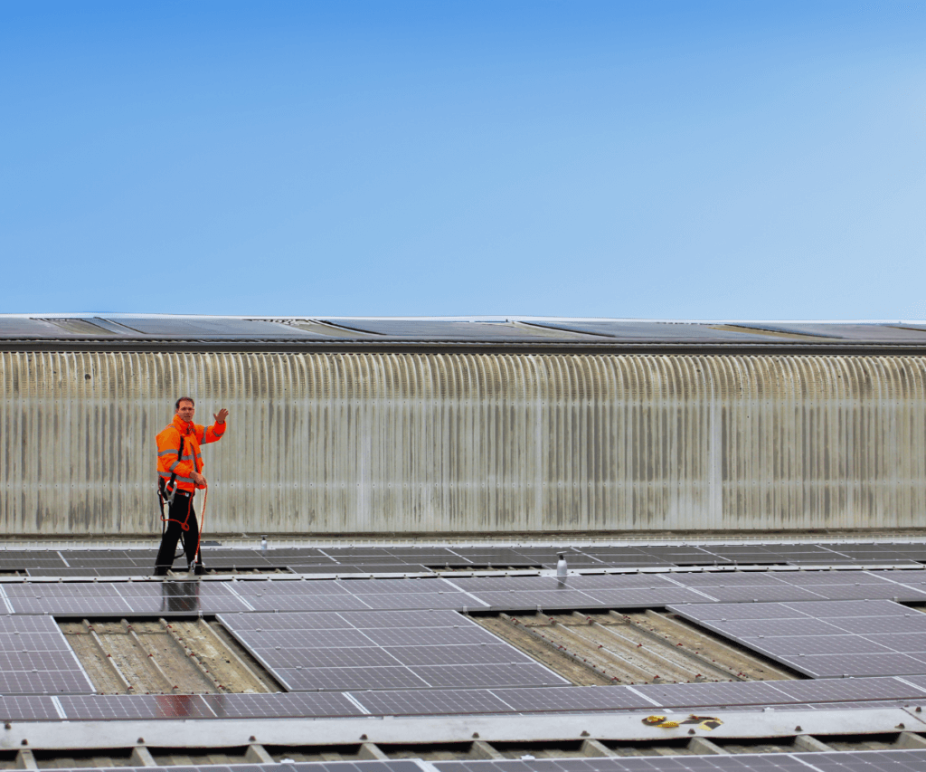 A man waving from above a solar panel roof installation.